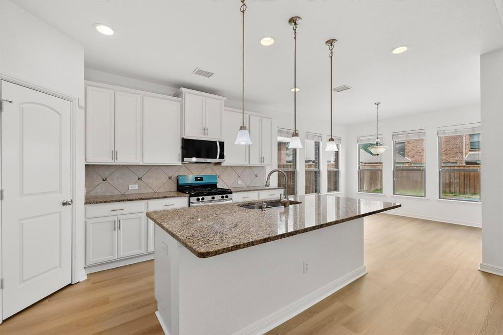 174 Hampton Drive Fate, TX 75087 - Photo 9 of 40 a large kitchen with kitchen island a large counter top stainless steel appliances and a wooden floor