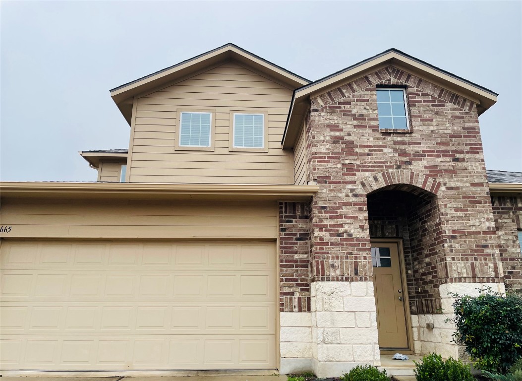 View of front facade with brick siding, a garage, and driveway