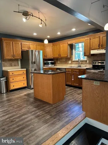 a kitchen with stainless steel appliances granite countertop wooden cabinets a refrigerator a sink a stove and a wooden floors