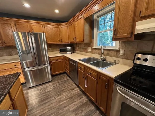 a kitchen with stainless steel appliances granite countertop a table chairs and a wooden floor