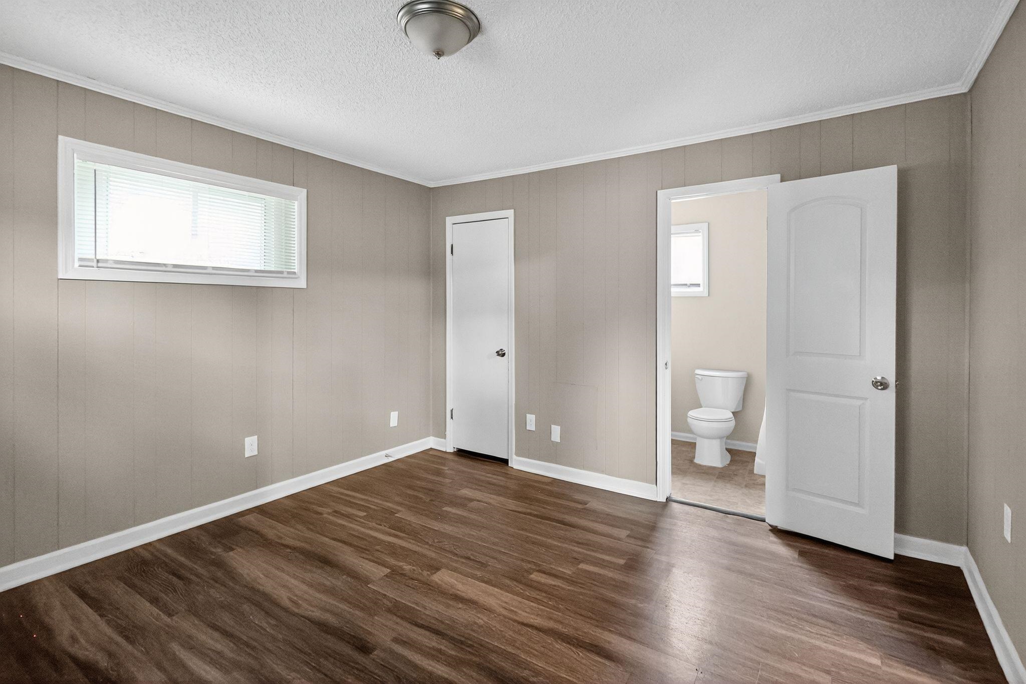 1563 Flamingo Road Memphis, TN 38117 - Photo 14 of 33 Unfurnished bedroom featuring crown molding, dark wood finished floors, a textured ceiling, connected bathroom, and wooden walls