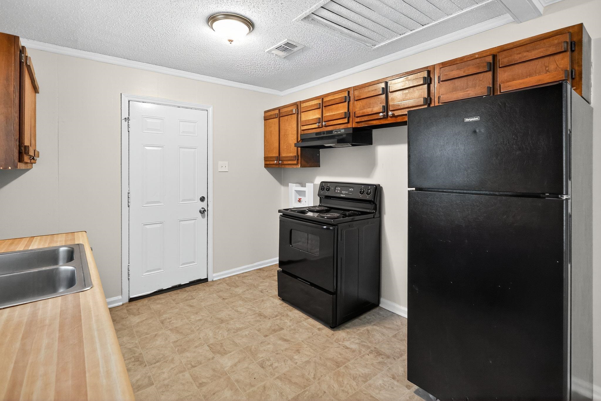 1563 Flamingo Road Memphis, TN 38117 - Photo 4 of 33 Kitchen featuring black appliances, brown cabinets, a textured ceiling, ornamental molding, and light countertops
