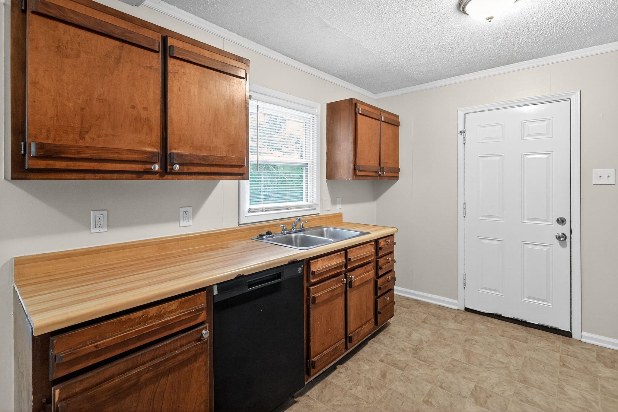 1563 Flamingo Road Memphis, TN 38117 - Photo 5 of 33 Kitchen with crown molding, dishwasher, brown cabinets, light countertops, and a textured ceiling