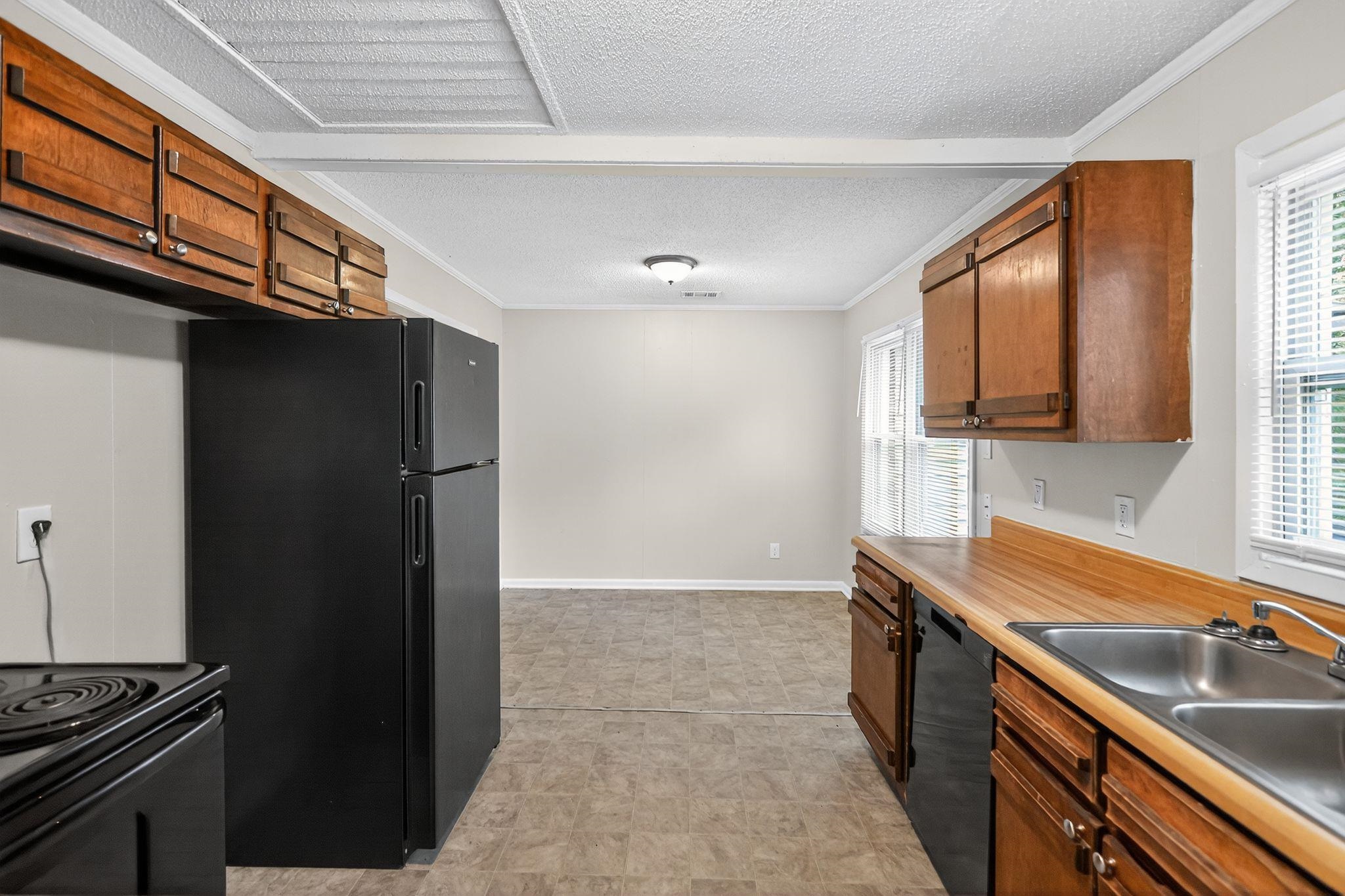 1563 Flamingo Road Memphis, TN 38117 - Photo 6 of 33 Kitchen featuring brown cabinetry, black appliances, light countertops, ornamental molding, and a textured ceiling
