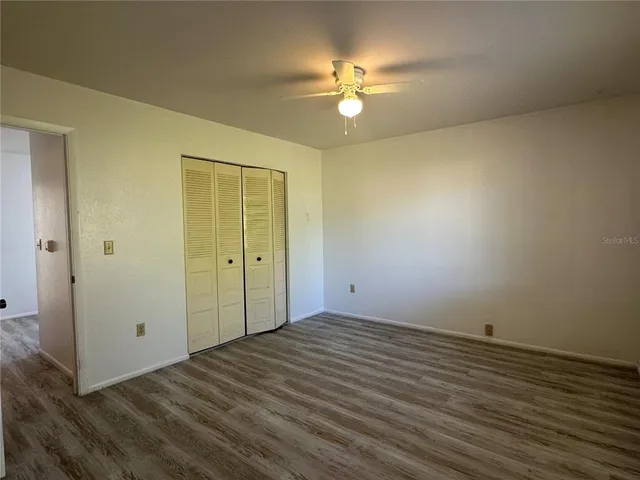 an empty room with a chandelier fan and wooden floor