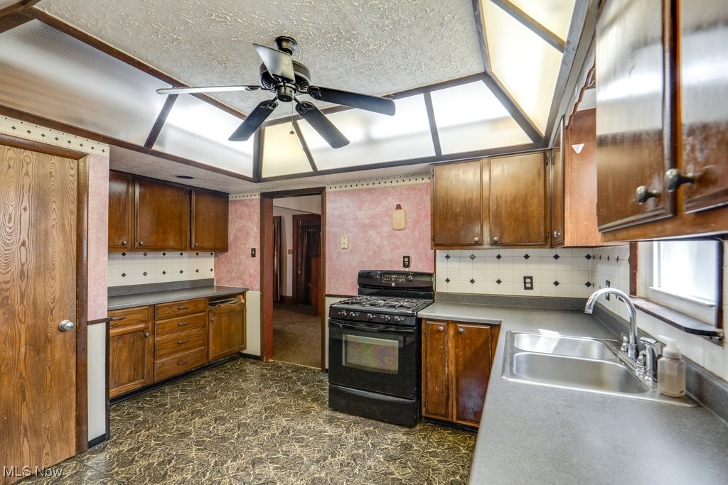 516 Floyd Street Akron, OH 44310 - Photo 14 of 50 Kitchen with black gas range oven, ceiling fan, brown cabinetry, wallpapered walls, and tasteful backsplash