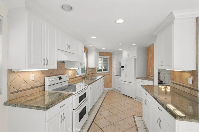 a large white kitchen with a stove a sink a refrigerator and white cabinets