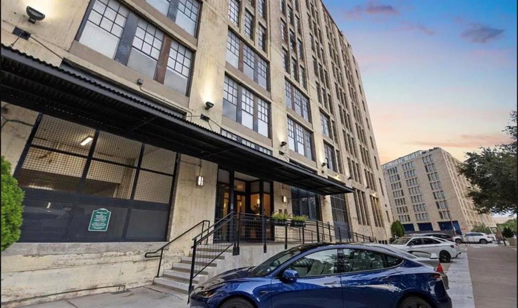 1122 Jackson Street, Unit 514 Dallas, TX 75202 - Photo 2 of 40 Multi-story building featuring a prominent entrance with a black metal awning, exterior wall sconces, and a concrete staircase with black railings