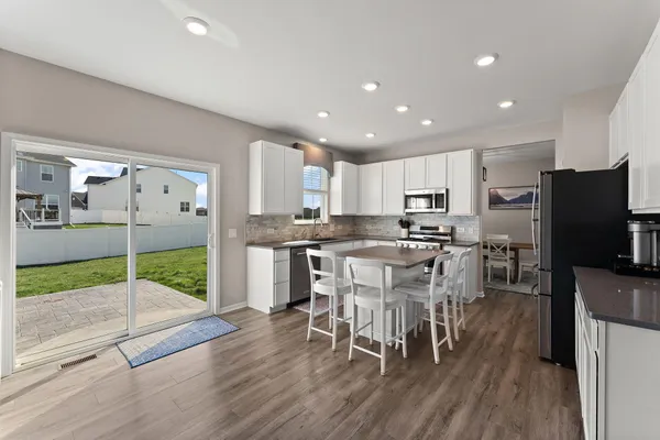 a kitchen with stainless steel appliances granite countertop a refrigerator a microwave a stove a sink a dining table and chairs with wooden floor