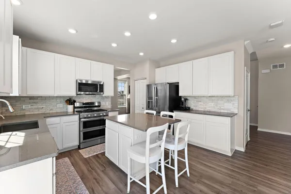 a kitchen with stainless steel appliances granite countertop a stove top oven a sink dishwasher a refrigerator and white cabinets with wooden floor