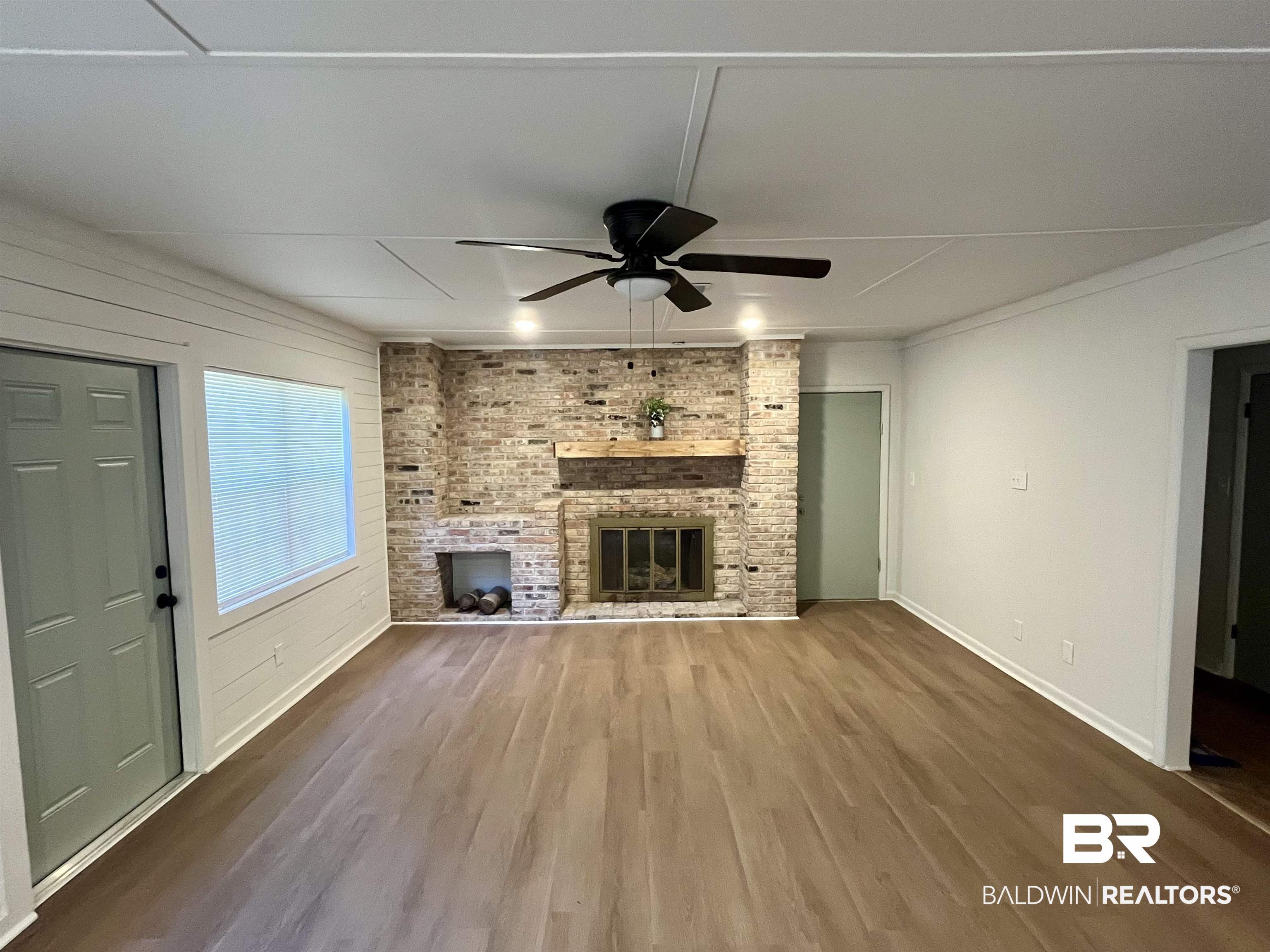 3105 Bryant Road Mobile, AL 36605 - Photo 18 of 39 Spacious interior featuring a brick fireplace with a wood mantle, wood-finish flooring, a ceiling fan, and white shiplap wall accents