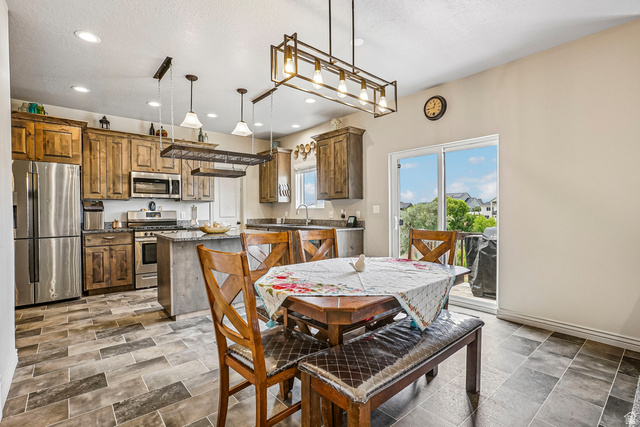 203 North 1900th Street West Mapleton, UT 84664 - Photo 7 of 48 Kitchen and dining area featuring wood-finish flooring, custom cabinetry, stainless steel appliances, a center island with countertop seating, and a sliding glass door