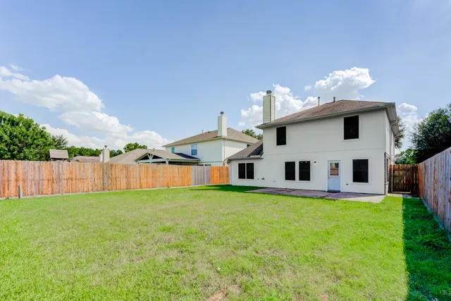 a white house that has a big yard with plants and large trees