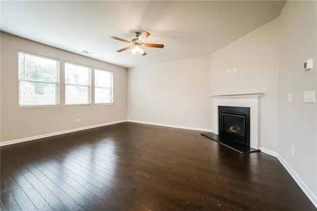 an empty room with wooden floor chandelier fan and windows