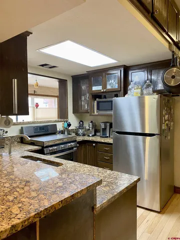 a kitchen with kitchen island granite countertop a refrigerator a sink a stove and wooden cabinets