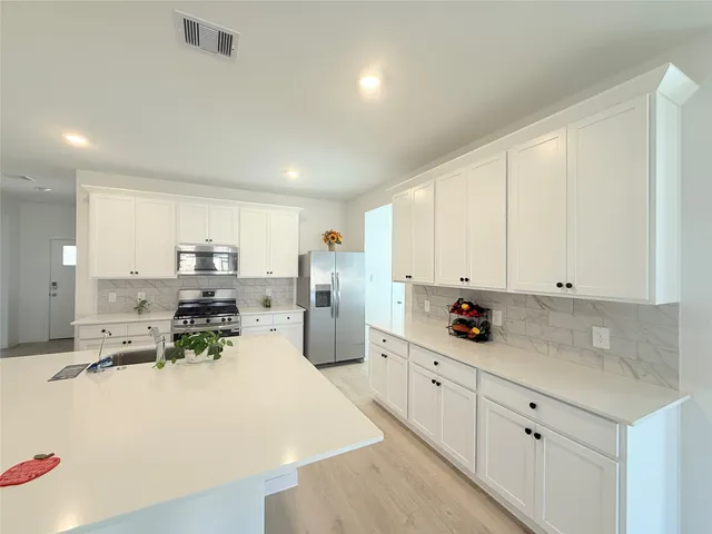 a kitchen with stainless steel appliances a sink a stove and white cabinets