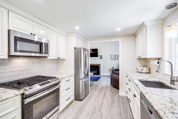 a kitchen with stainless steel appliances kitchen island granite countertop a stove a sink dishwasher a refrigerator and a microwave oven with wooden floor