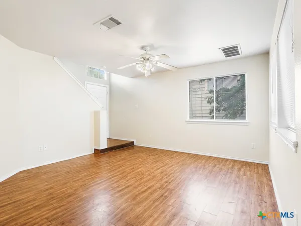 an empty room with wooden floor chandelier fan and windows