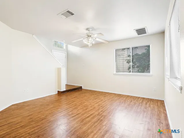 an empty room with wooden floor chandelier fan and windows