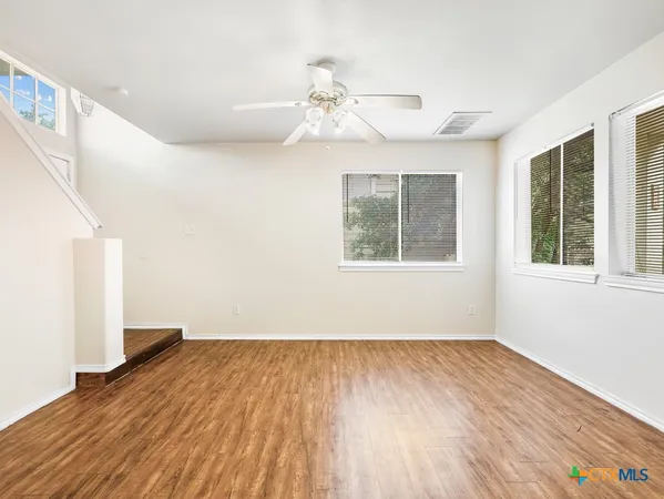 a view of empty room with wooden floor and fan