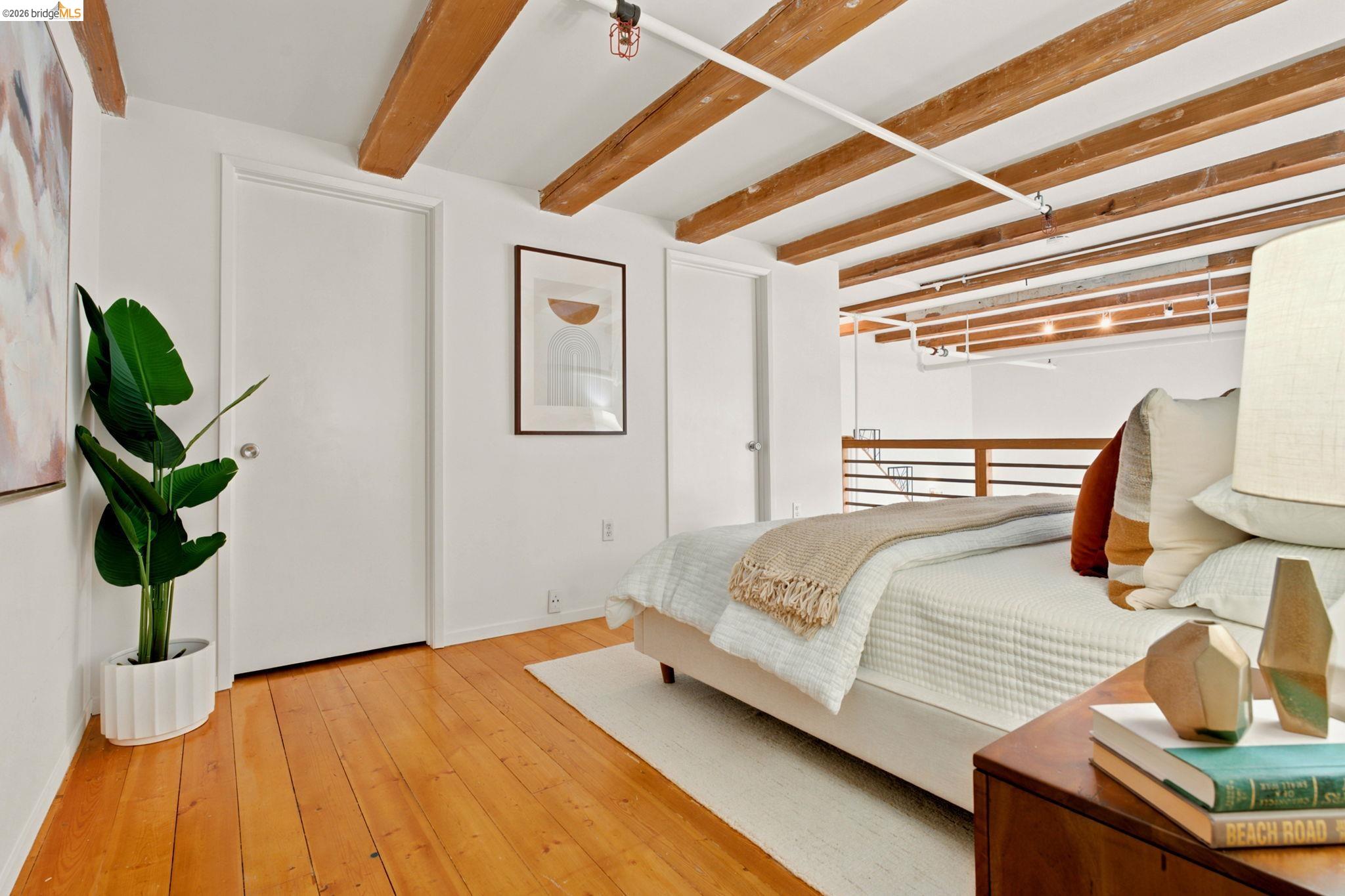 1920 Union Street, Unit 9 Oakland, CA 94607 - Photo 22 of 35 Exposed wood beam ceiling in a loft-style room featuring wood-finish flooring, white walls, and a modern horizontal railing