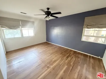 an empty room with wooden floor fan and windows