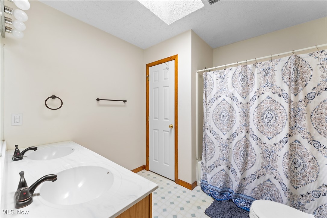 6272 Merwin Chase Road Brookfield, OH 44403 - Photo 18 of 38 Bathroom featuring a textured ceiling, a skylight, toilet, vanity, and tile patterned flooring