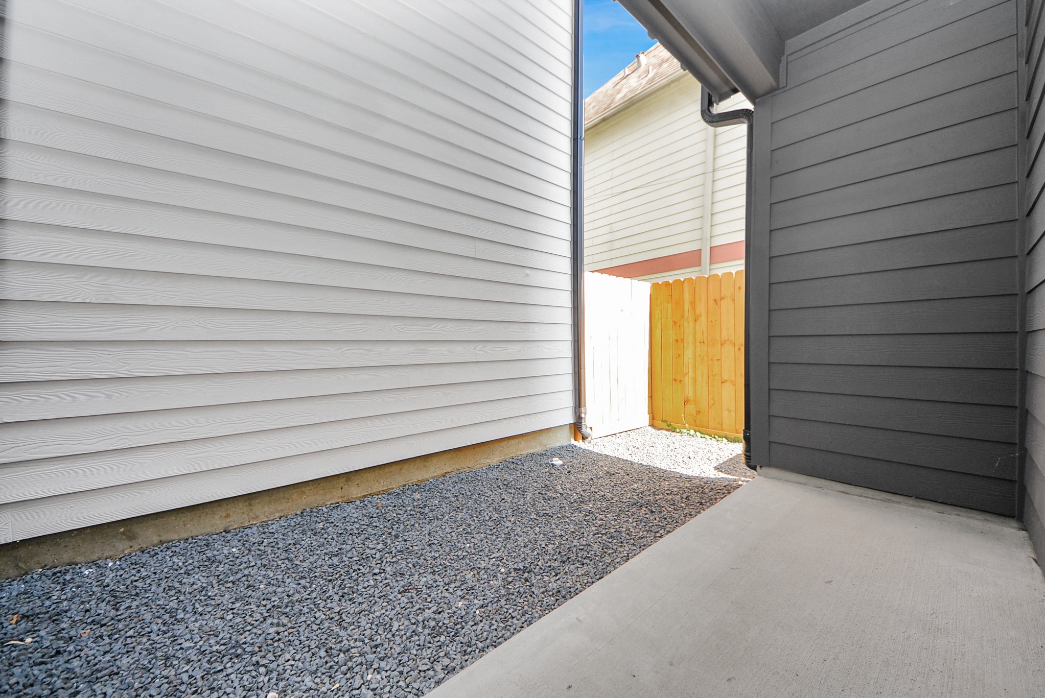 927 Fisher Street, Unit B Houston, TX 77018 - Photo 42 of 47 Step into this narrow outdoor side area between homes, with gravel ground and siding walls. A wooden fence at the end provides privacy while maintaining a clean and orderly appearance.