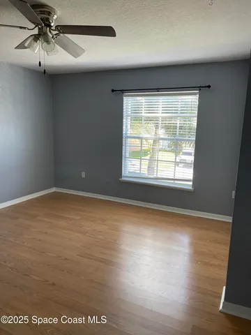 an empty room with wooden floor fan and windows