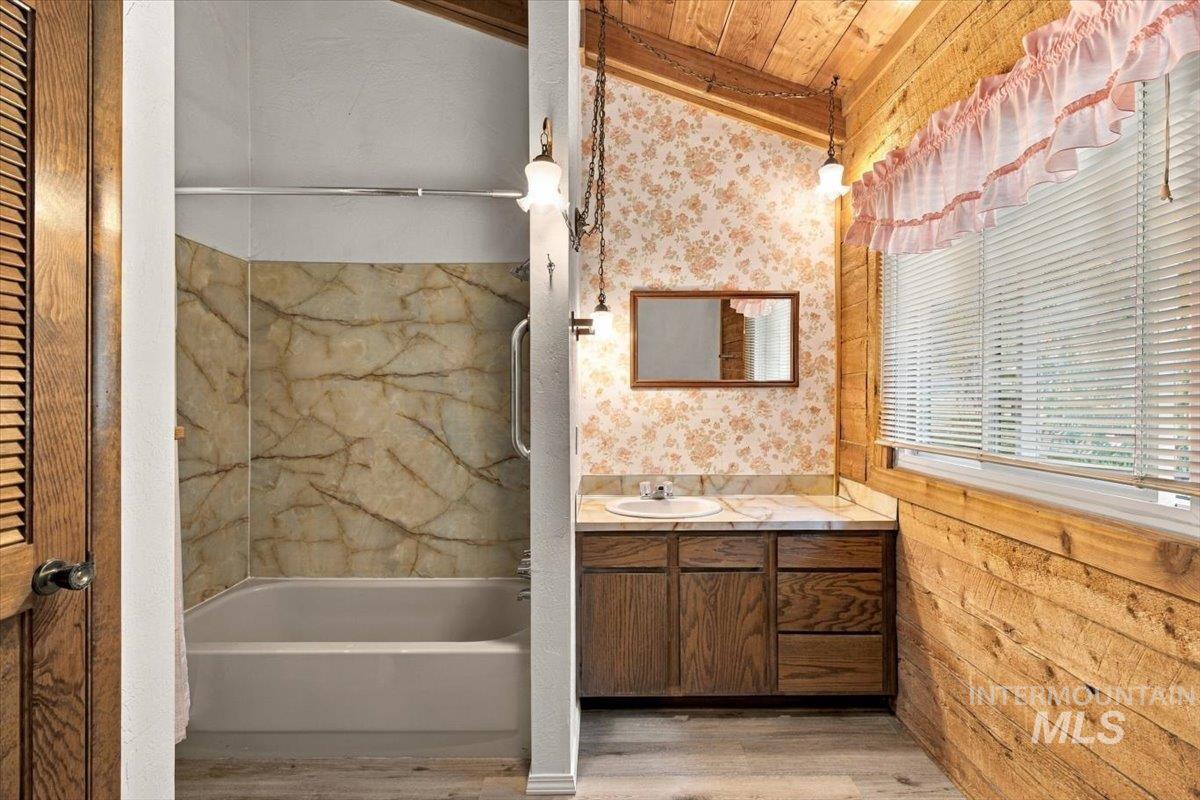 10201 Willis Road Middleton, ID 83644 - Photo 20 of 38 Bathroom featuring wood-finish walls, a built-in vanity with a countertop and undermount sink, and a tub/shower combination with a grab bar