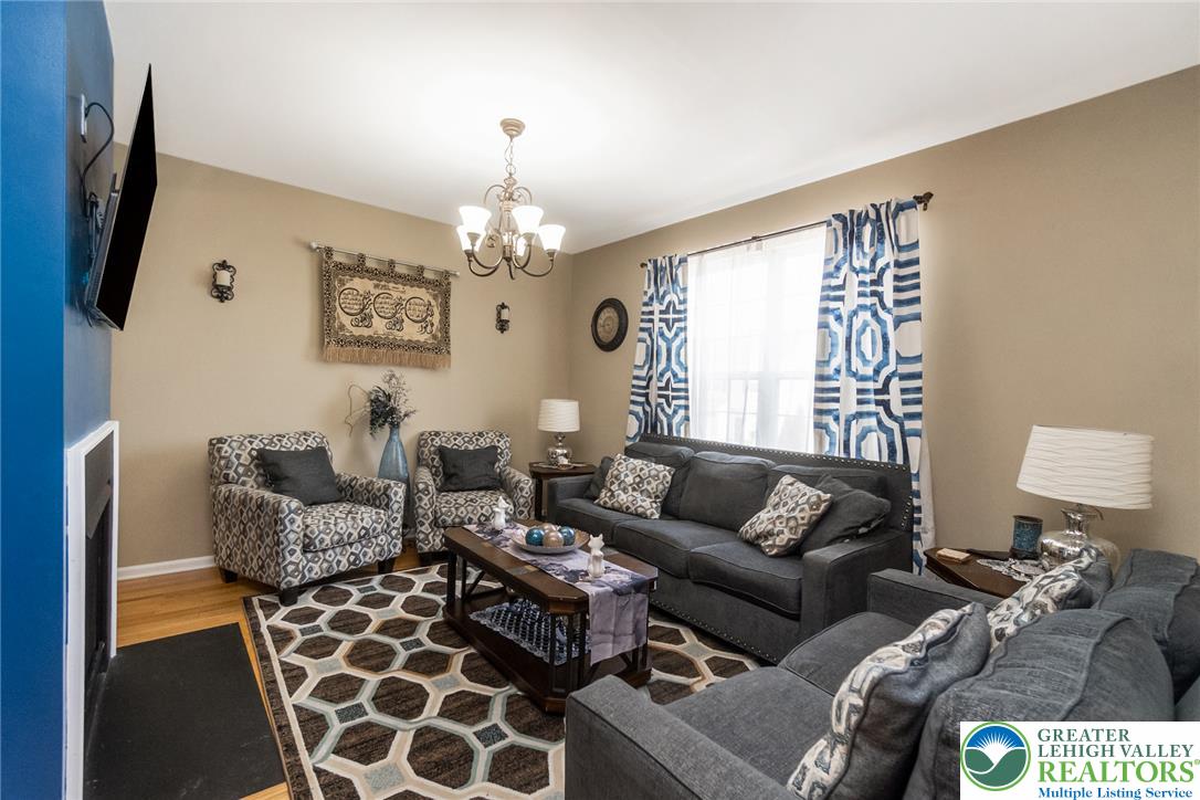3566 Penfield Way Nazareth, PA 18064 - Photo 25 of 47 A welcoming living room featuring hardwood flooring, a statement chandelier, and a cozy fireplace, perfect for gatherings.