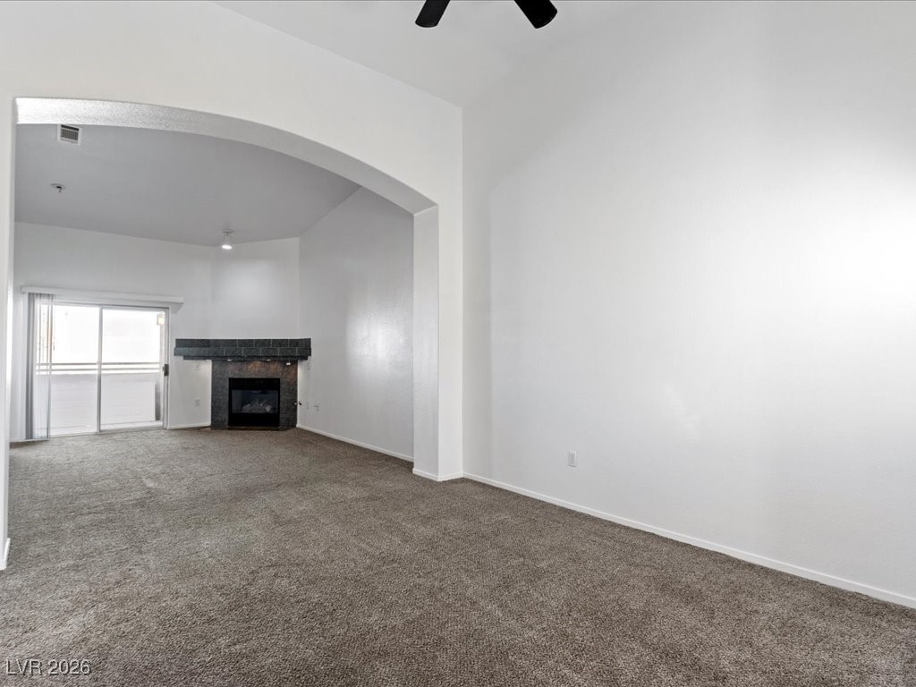 8725 West Flamingo Road, Unit 235 Las Vegas, NV 89147 - Photo 4 of 22 Unfurnished living room with carpet, a tile fireplace, a ceiling fan, and arched walkways