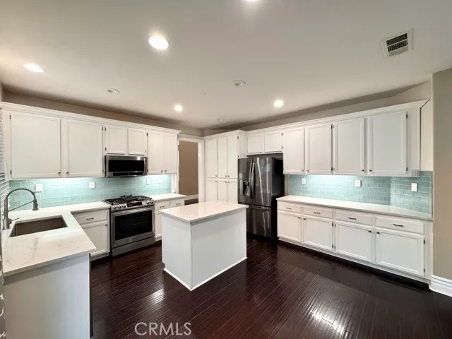 a large kitchen with stainless steel appliances granite countertop a stove top oven a refrigerator a sink and dishwasher with wooden floor