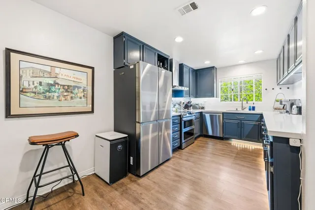 a kitchen with stainless steel appliances kitchen island granite countertop a refrigerator a stove a sink dishwasher and wooden cabinets with wooden floor