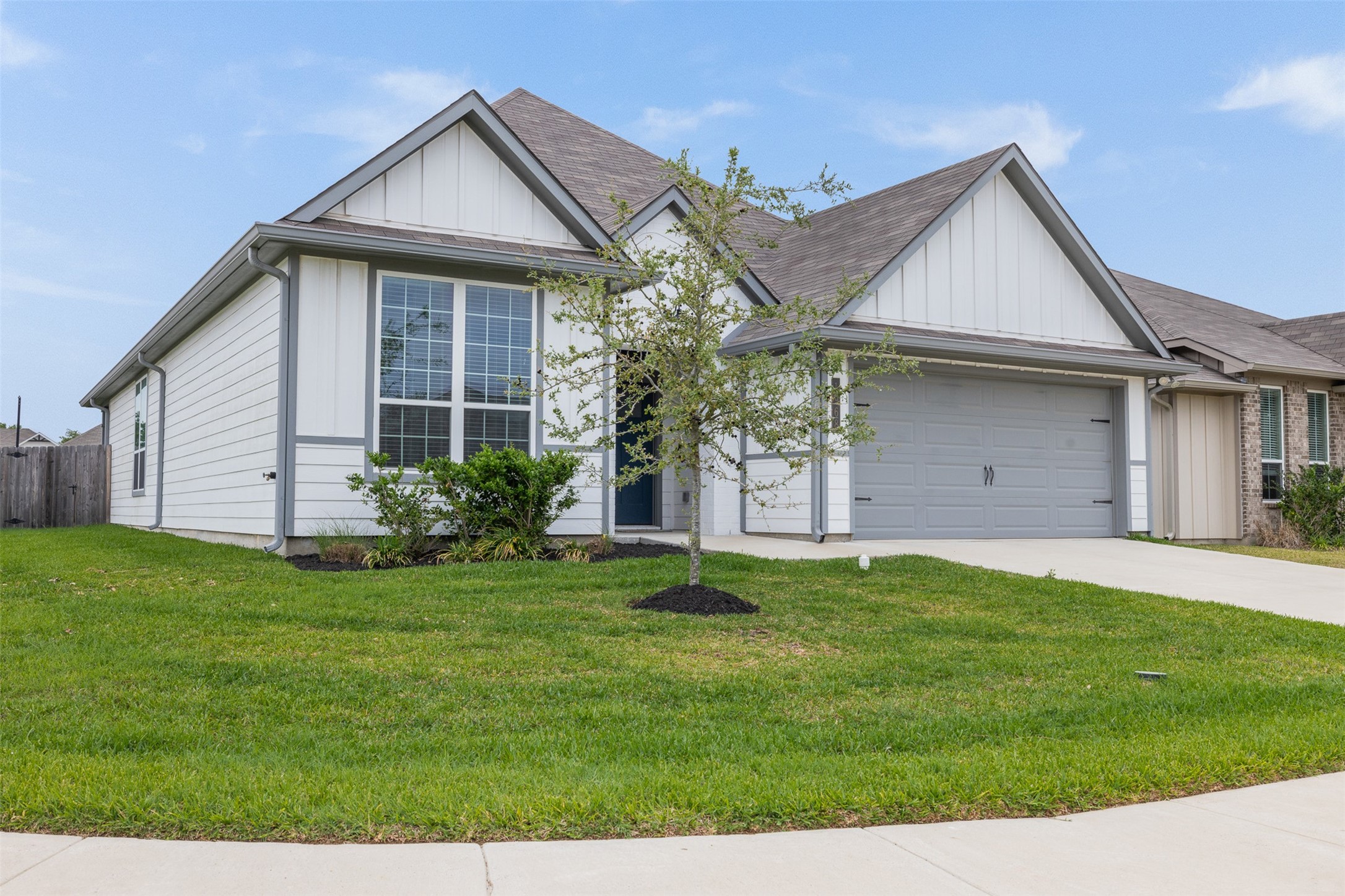 1968 Chief Street Bryan, TX 77807 - Photo 26 of 27 This photo features a modern single-story home with a gabled roof and a two-car garage. The house has a bright exterior with large front windows and is surrounded by a well-maintained lawn. A concrete driveway leads to the garage, enhancing curb appeal.