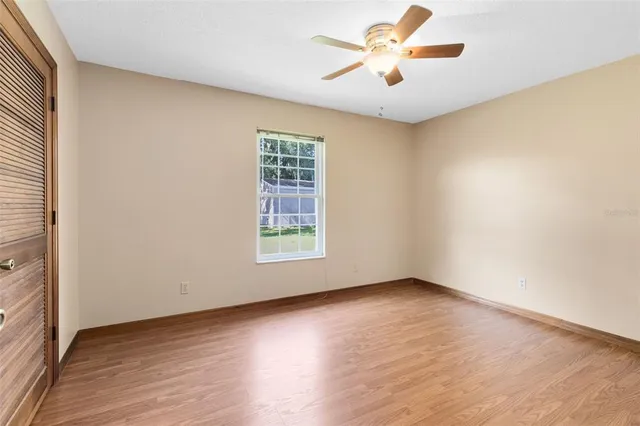 an empty room with wooden floor chandelier fan and windows
