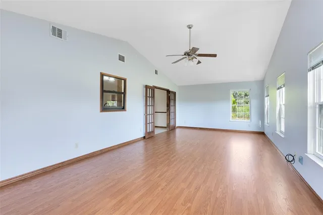 an empty room with wooden floor chandelier fan and windows