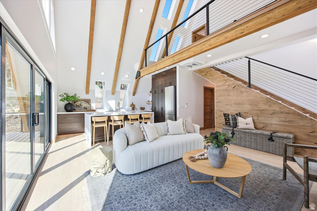 1833 Pine Loop Road Coalville, UT 84017 - Photo 3 of 26 Vaulted ceilings with exposed wood beams, a modern kitchen island with seating, wide plank wood-finish flooring, a wall of glass sliding doors, and a staircase featuring a wood plank wall and cable railing
