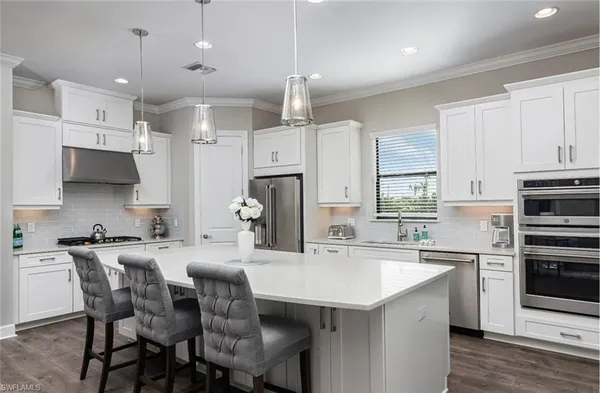 a kitchen with stainless steel appliances a sink a stove a refrigerator cabinets and chairs