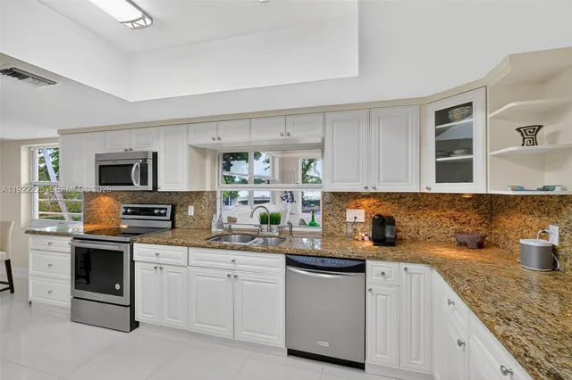 a kitchen with granite countertop a sink stainless steel appliances white cabinets and window