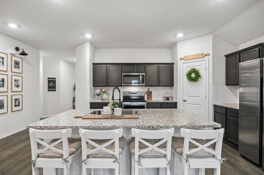 1107 Ringgold Road Forney, TX 75126 - Photo 11 of 27 Spacious kitchen featuring a large island with seating, dark wood cabinetry, stainless steel appliances, speckled stone countertops, and wood-finish flooring
