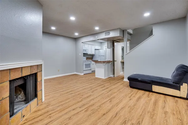 a living room with stainless steel appliances furniture a fireplace and a wooden floor