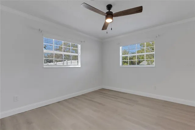 an empty room with wooden floor ceiling fan and windows