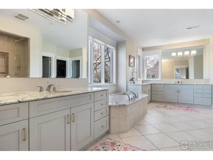 a spacious bathroom with a granite countertop double vanity sink a mirror a bathtub and window