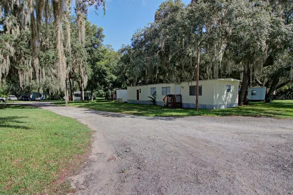a view of a white house with a yard and large trees