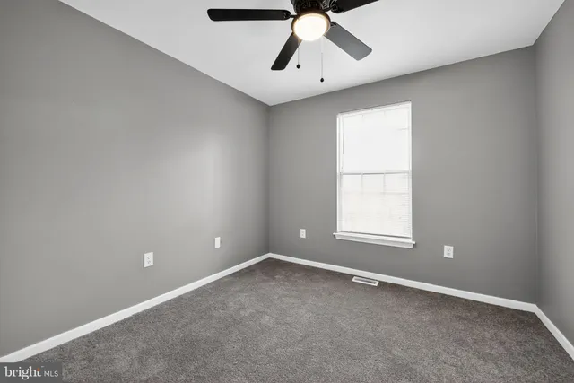 an empty room with chandelier fan and windows