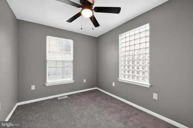 an empty room with chandelier fan and windows