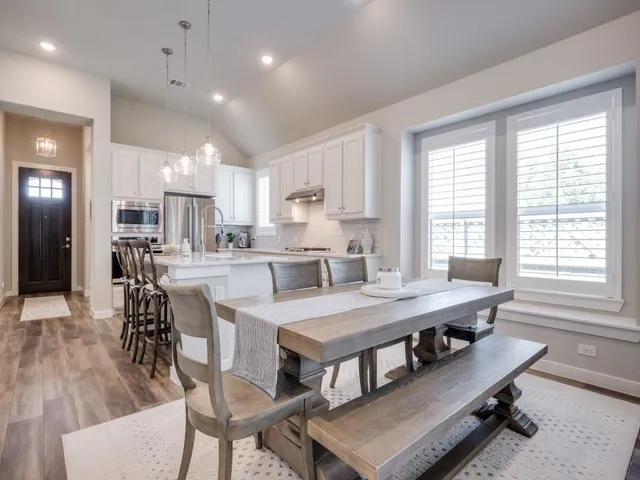 a room with a table chairs wooden floor and appliances