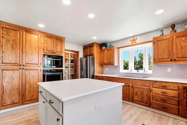 a view of a kitchen with kitchen island stainless steel appliances wooden floor and a window