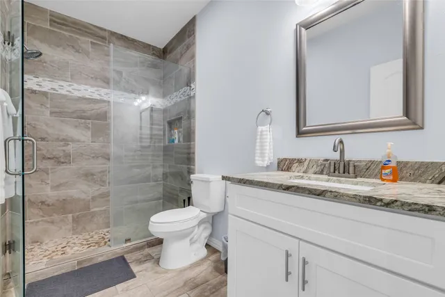 a bathroom with a granite countertop sink a toilet a mirror and shower